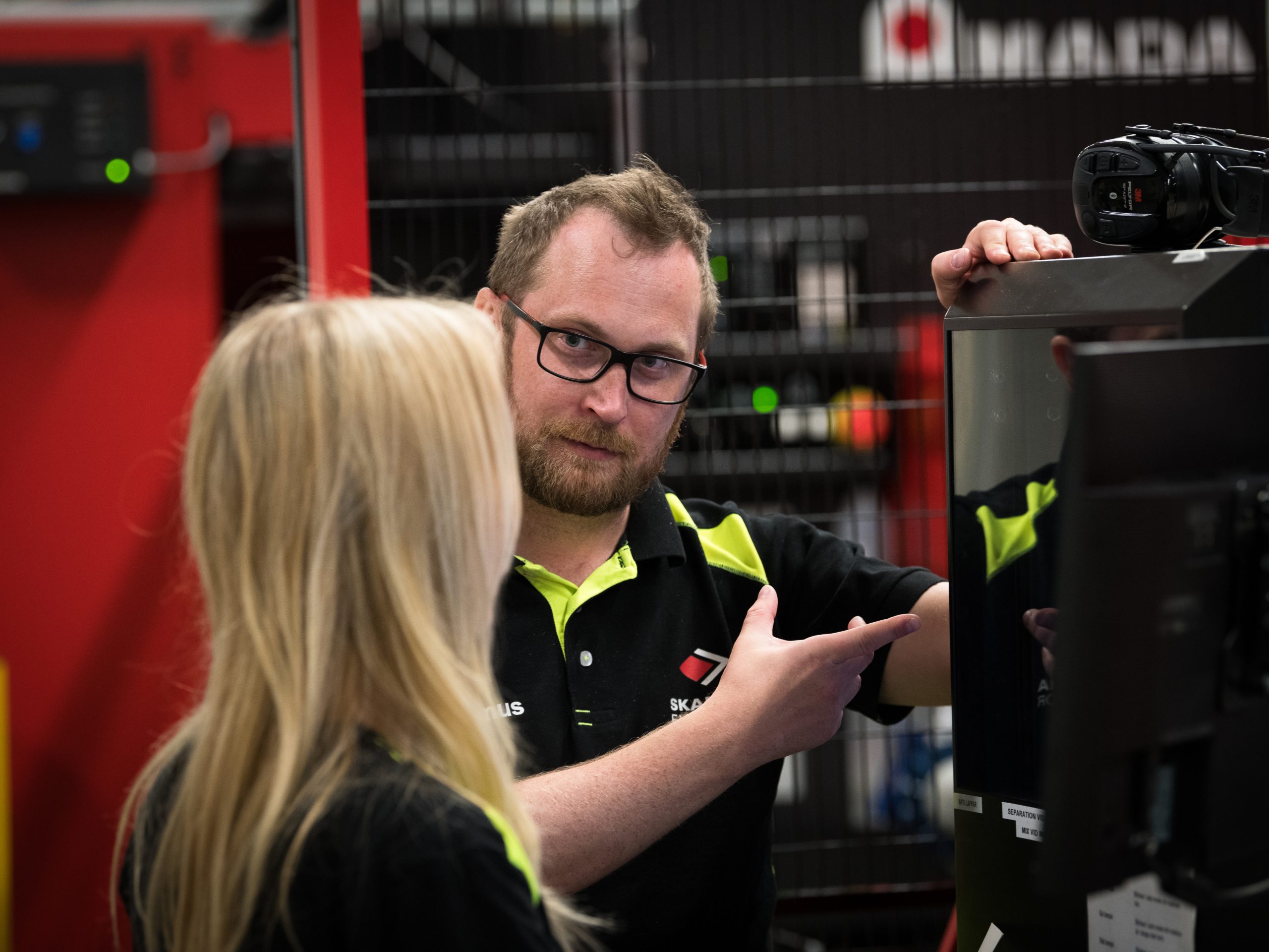 A man in a working uniform demonstrates a product for a woman with blonde hair.
