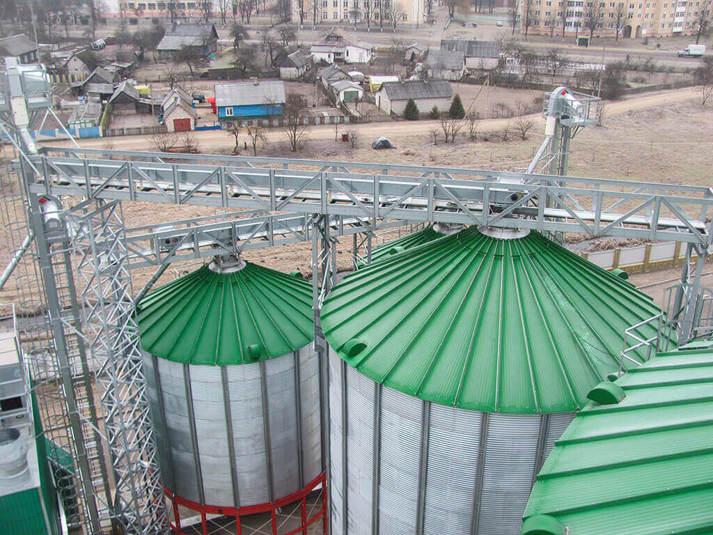 Industrial silos system with green a roof and buildings in the background.