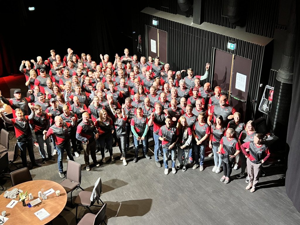 Group photo of Skandia Elevator employees in factory setting.