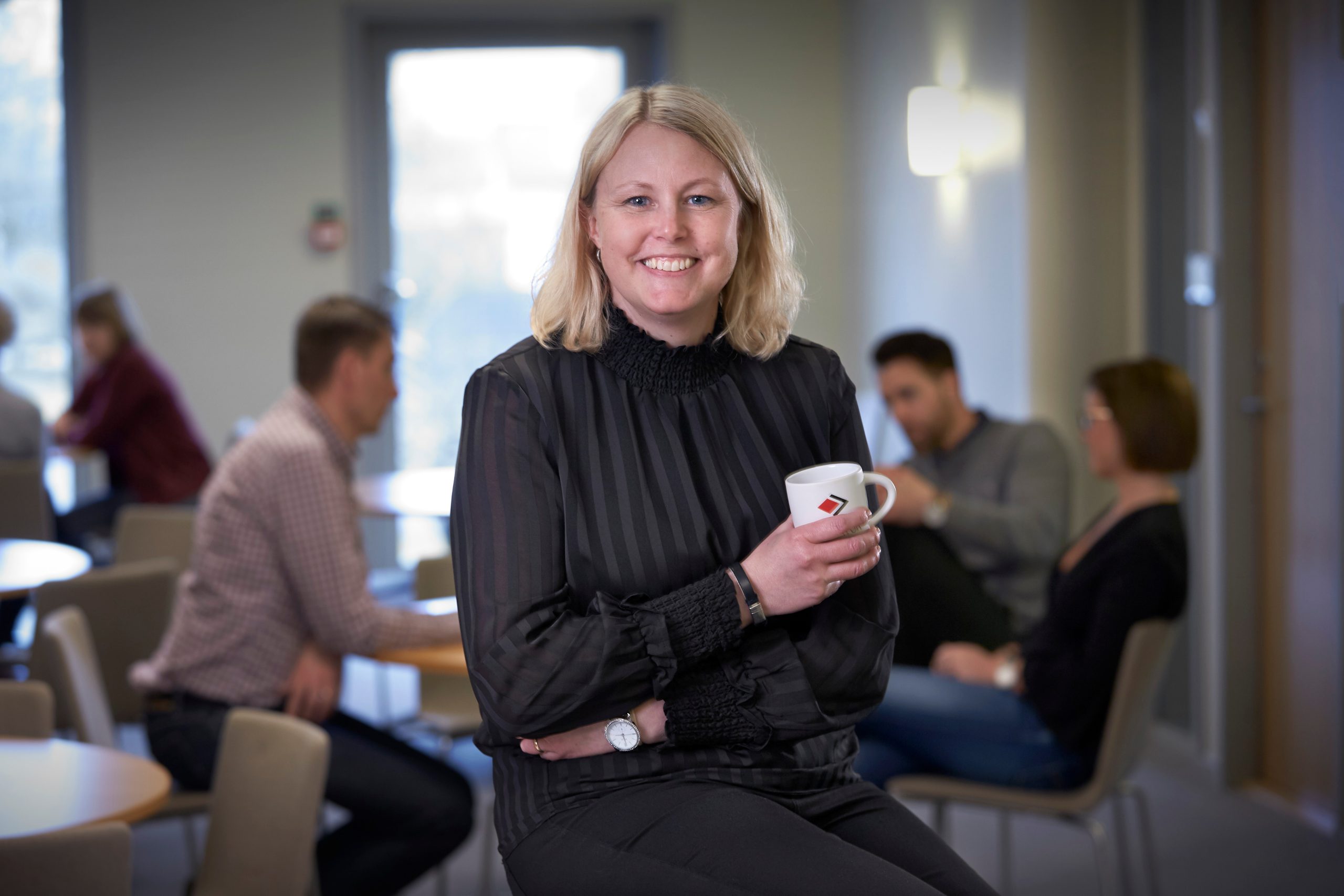 Woman in a black blouse holding a coffee mug and smiling.